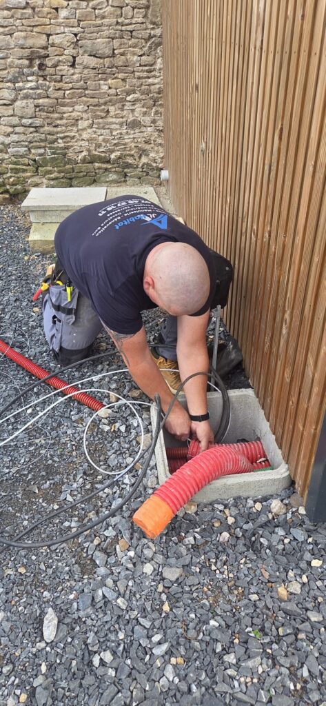 Électricité en Normandie : technicien AJL HABITAT en intervention, passage de gaines et raccordements électriques sur chantier extérieur.