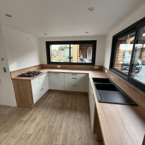 Menuiserie intérieure en Normandie : cuisine équipée avec plan de travail bois, évier noir et meubles sur mesure, pose soignée par AJL HABITAT.