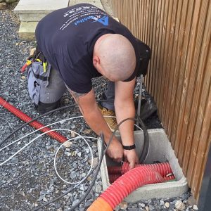Électricité en Normandie : technicien AJL HABITAT en intervention, passage de gaines et raccordements électriques sur chantier extérieur.